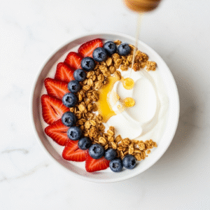 A-beautiful-white-bowl-of-Greek-yogurt-artfully-topped-with-fresh-strawberries-blueberries-and-crunchy-granola-from-a-top-down-view.