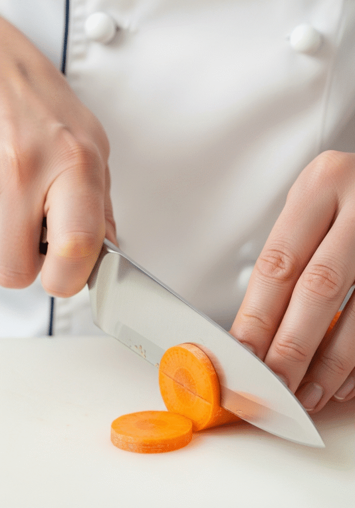 A close-up of a person's hands safely holding a chef's knife with a pinch grip and holding a carrot with a claw grip.