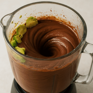 A glass blender in action, transforming avocados and cocoa powder into a smooth and creamy chocolate avocado mousse.