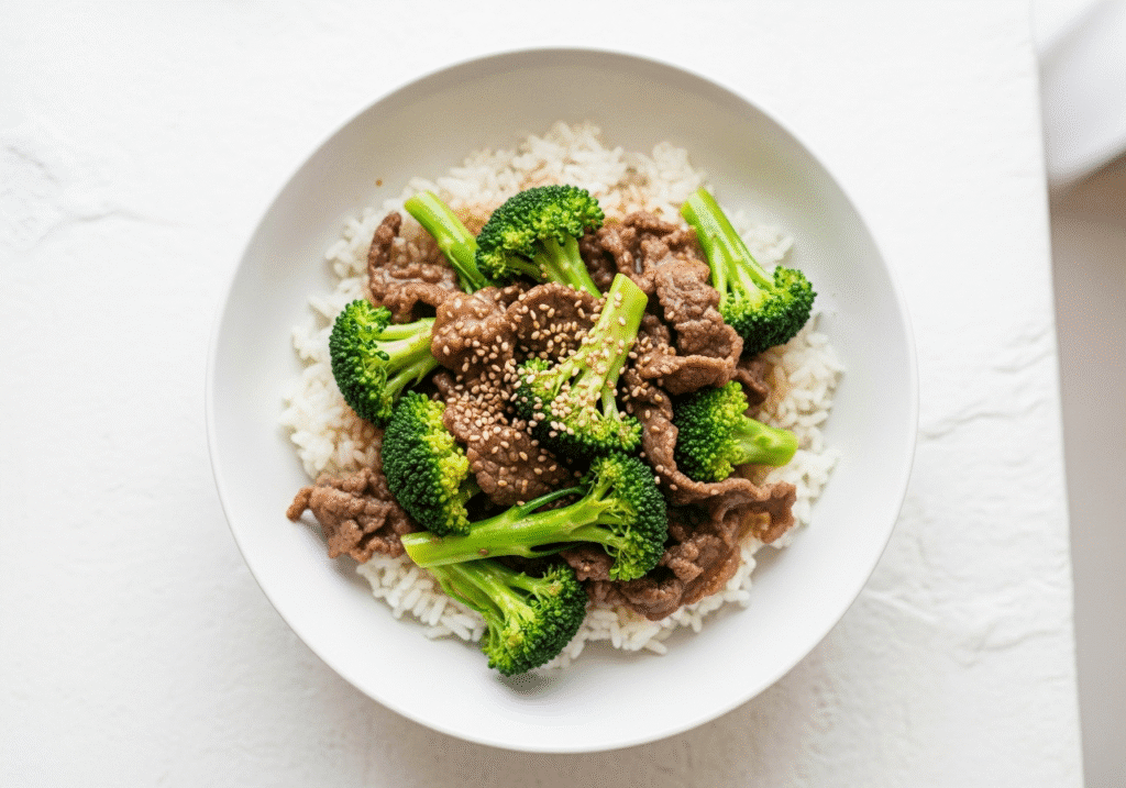 A simple white bowl with the finished easy beef and broccoli recipe served over a bed of white rice.